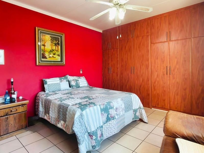 Spacious bedroom featuring extensive built-in wooden cupboards, a ceiling fan, and neutral tiled flooring.