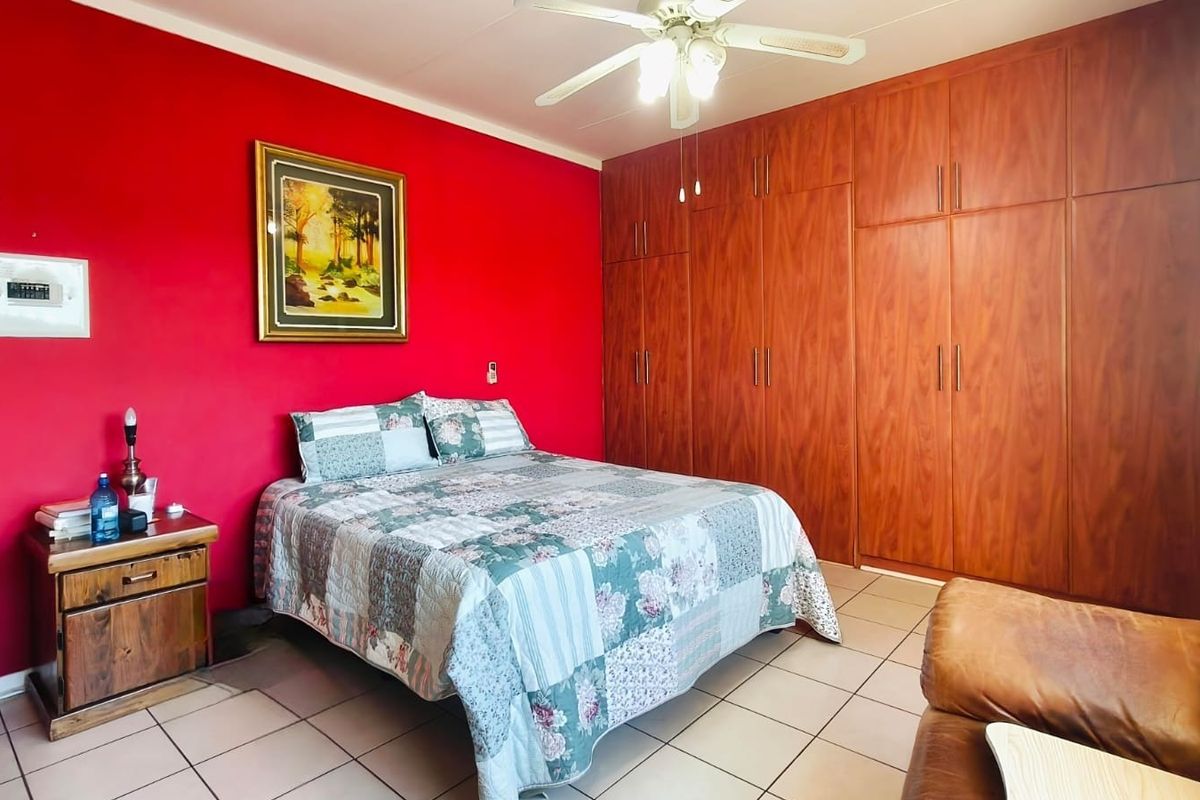 Spacious bedroom featuring extensive built-in wooden cupboards, a ceiling fan, and neutral tiled flooring.