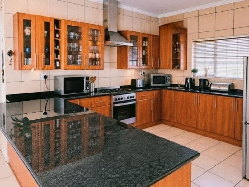 A well-maintained kitchen featuring wooden cabinetry, granite countertops, a stainless steel extractor fan, and a built-in oven with a tiled backsplash.