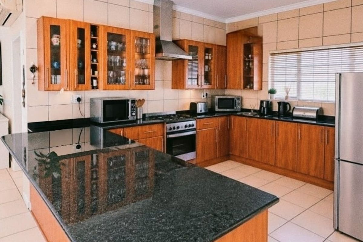 A well-maintained kitchen featuring wooden cabinetry, granite countertops, a stainless steel extractor fan, and a built-in oven with a tiled backsplash.