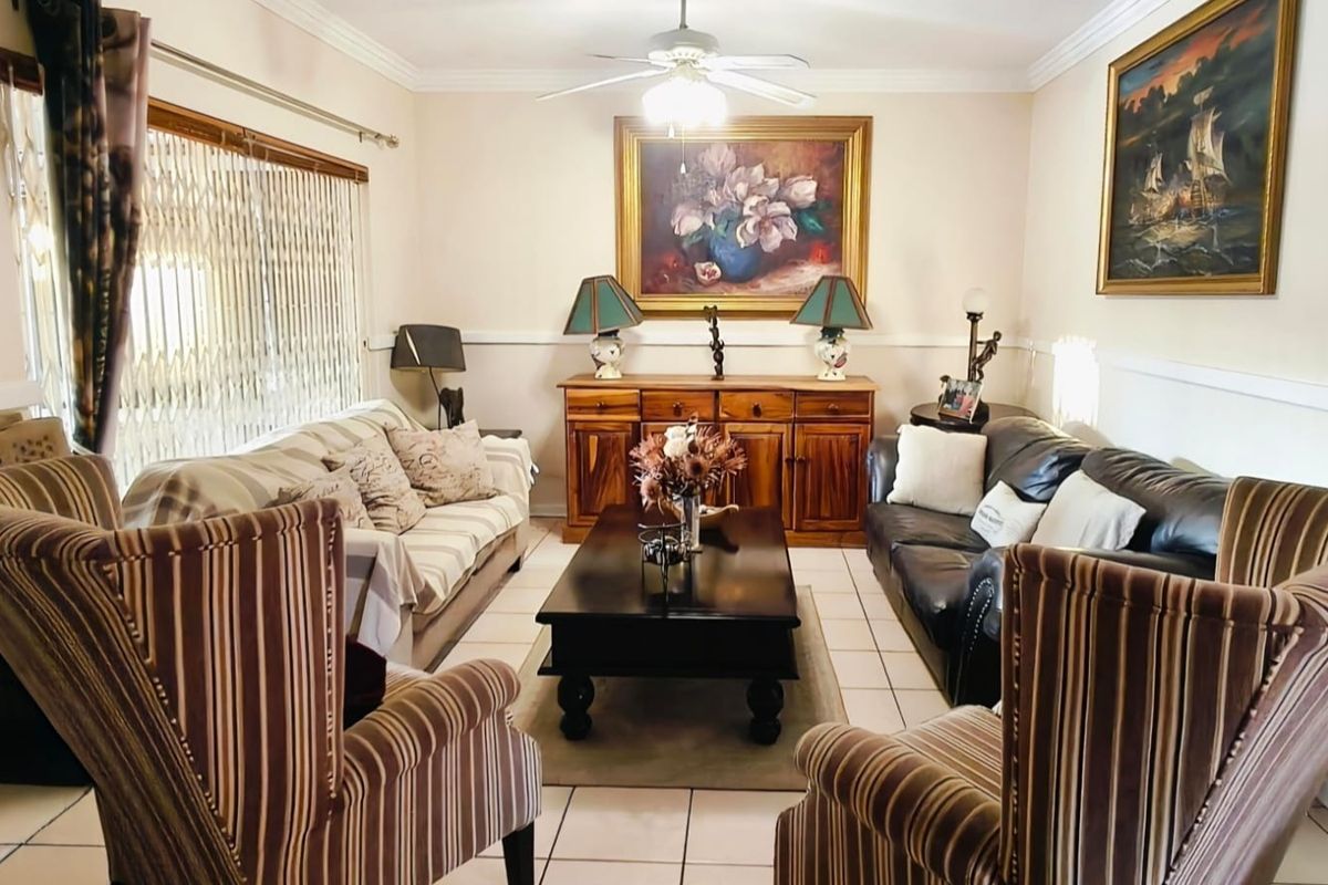 A comfortable living room featuring tiled flooring, a ceiling fan, and a decorative chair rail, providing a functional and traditional living space.