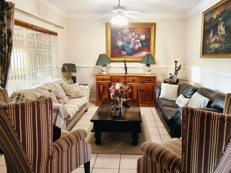 A comfortable living room featuring tiled flooring, a ceiling fan, and a decorative chair rail, providing a functional and traditional living space.