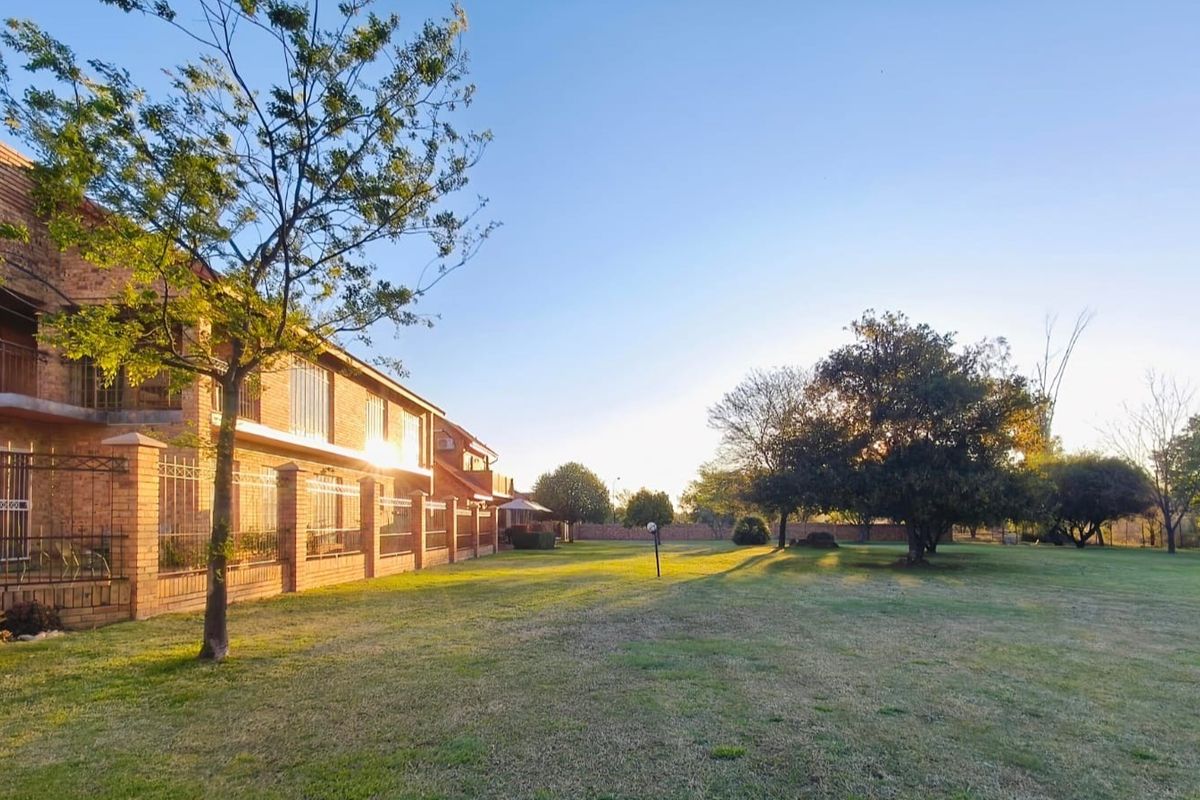 A view of the rear face brick townhouse facade featuring balconies with security bars, overlooking a spacious, well-maintained communal lawn area.