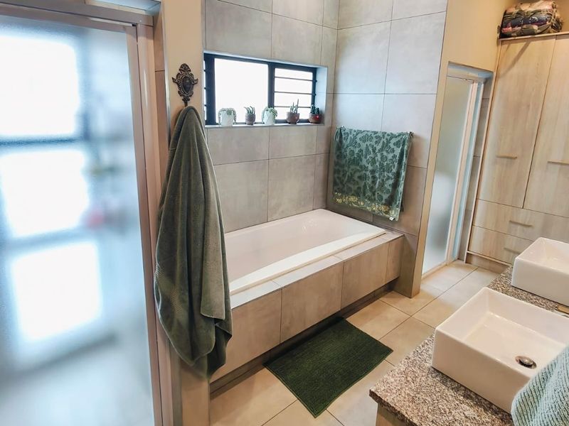 Modern bathroom featuring a built-in bathtub, dual vessel sinks with granite vanity, and neutral tiled finishes throughout.