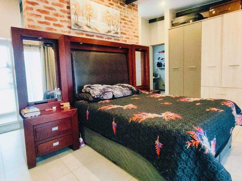Spacious bedroom featuring an exposed brick accent wall, extensive built-in cabinetry, and neutral tiled flooring.