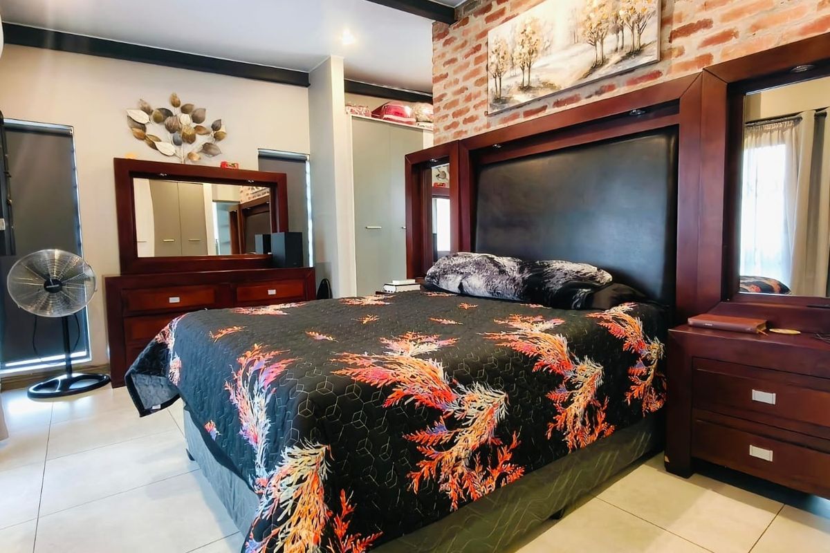 Spacious bedroom featuring an exposed brick accent wall, built-in cabinetry, tiled flooring, and an integrated air conditioning unit.