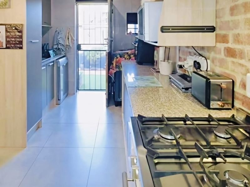 A functional kitchen featuring a gas hob, extractor fan, granite countertops, and an exposed brick feature wall, leading to an exterior door.