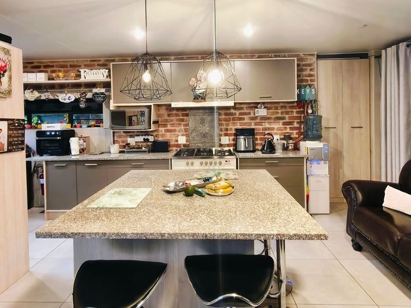 An open-plan kitchen featuring a central island with granite countertops, exposed brick backsplash, and modern cabinetry, seamlessly integrated with the living area.