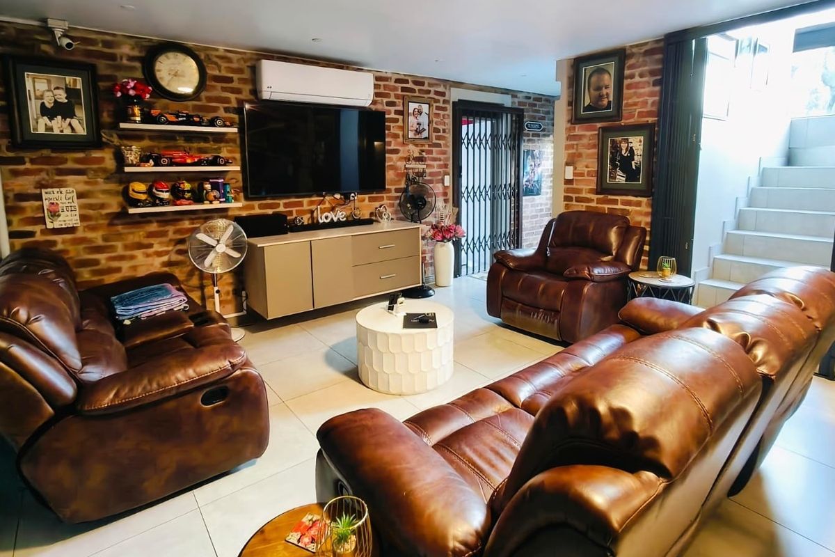 A comfortable living room featuring an exposed brick feature wall, tiled flooring, and a split-system air conditioner, with direct access to an internal staircase.