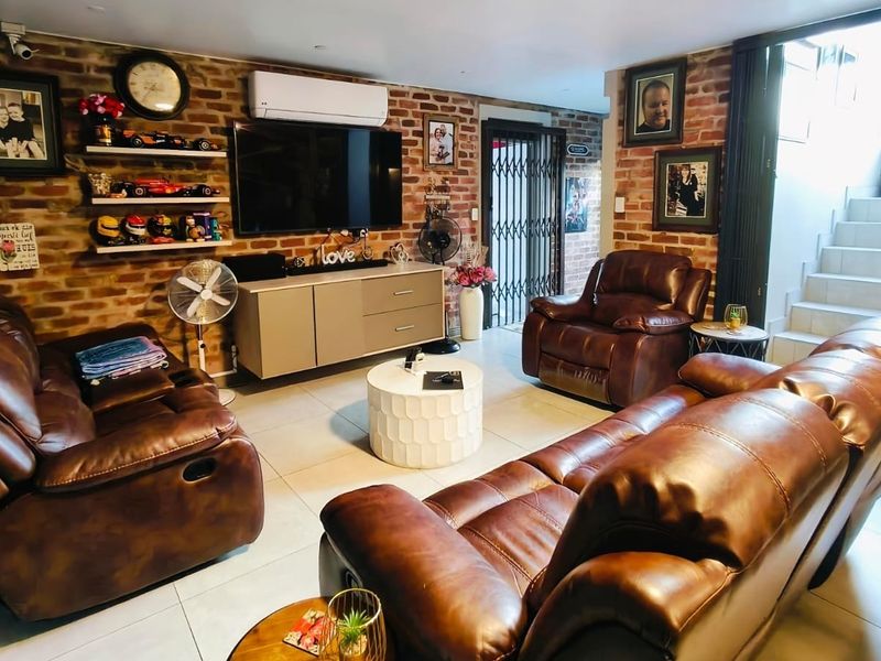 A comfortable living room featuring an exposed brick feature wall, tiled flooring, and a split-system air conditioner, with direct access to an internal staircase.
