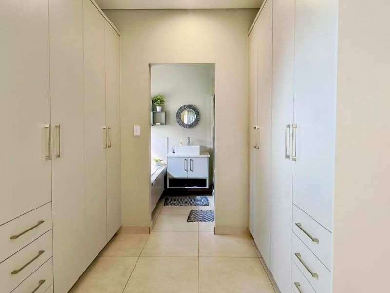 A clean, modern dressing area featuring extensive built-in cabinetry with sleek handles, leading through to an adjoining bathroom space with a vanity unit.