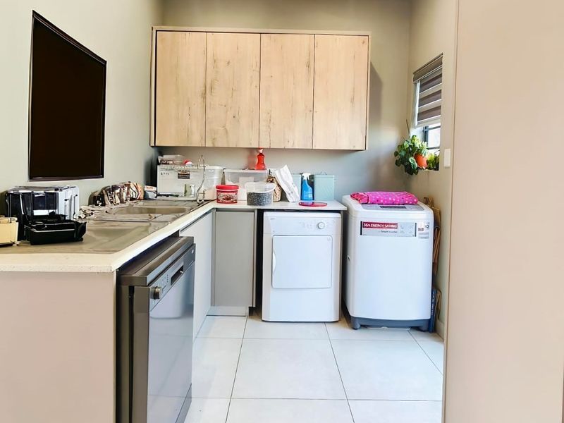 A functional laundry room featuring built-in cabinetry, laminate countertops, a sink, and tiled flooring, providing ample space for laundry appliances and storage.