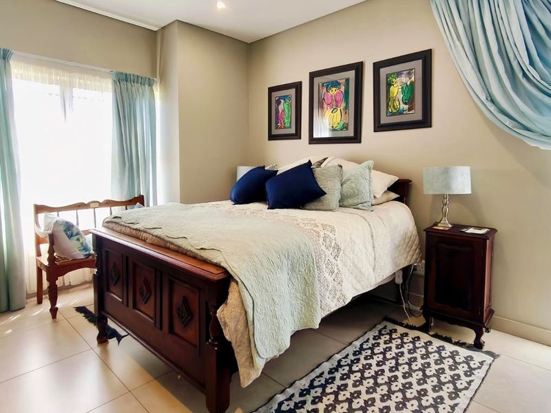 A well-maintained bedroom featuring neutral wall tones, tiled flooring, and natural light from large windows.
