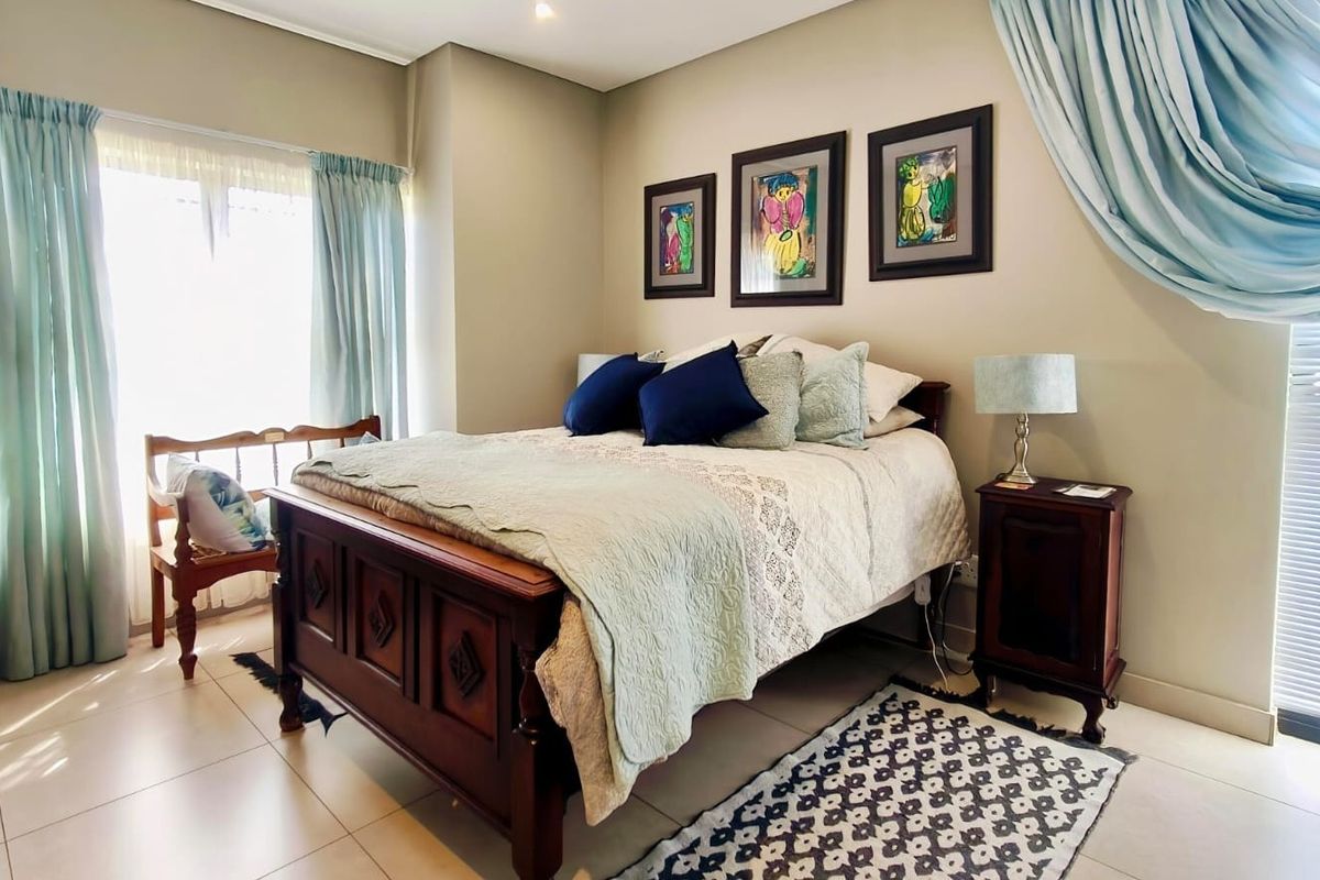 A well-maintained bedroom featuring neutral wall tones, tiled flooring, and natural light from large windows.
