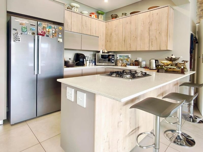 Modern kitchen featuring light wood-finish cabinetry, stone countertops, a central island with a gas hob, and tiled flooring.