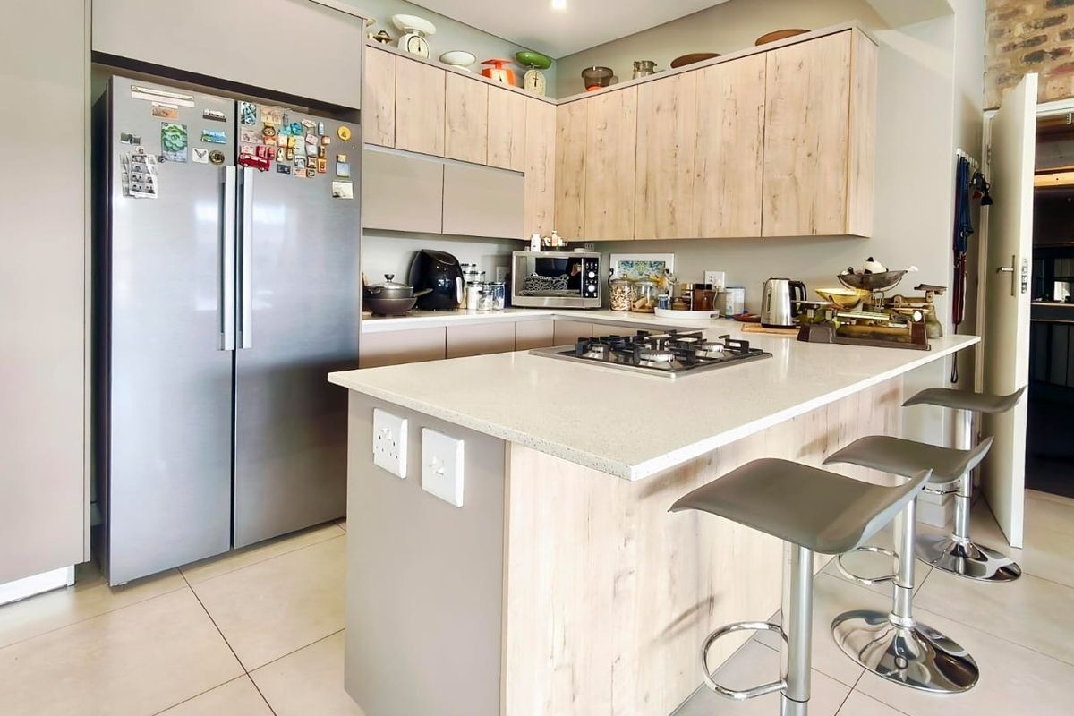 Modern kitchen featuring light wood-finish cabinetry, stone countertops, a central island with a gas hob, and tiled flooring.