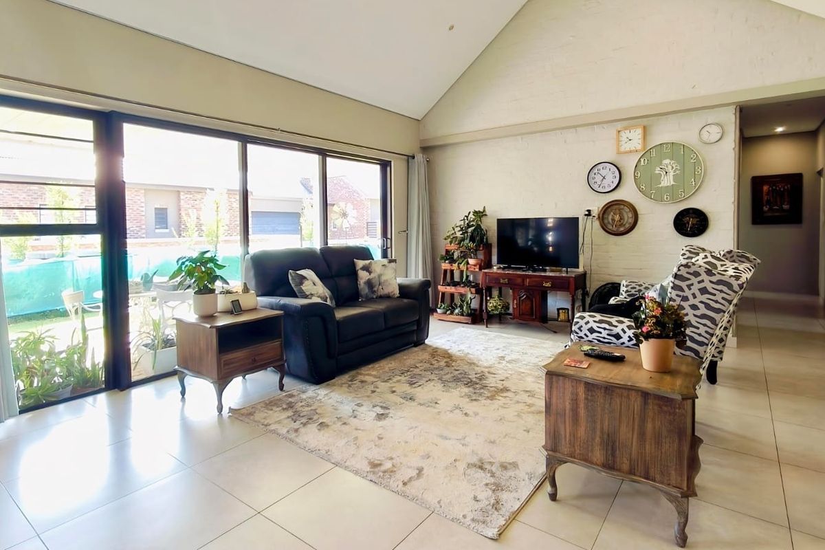 Spacious living room featuring a high vaulted ceiling, tiled flooring, and large sliding glass doors that provide ample natural light and garden access.