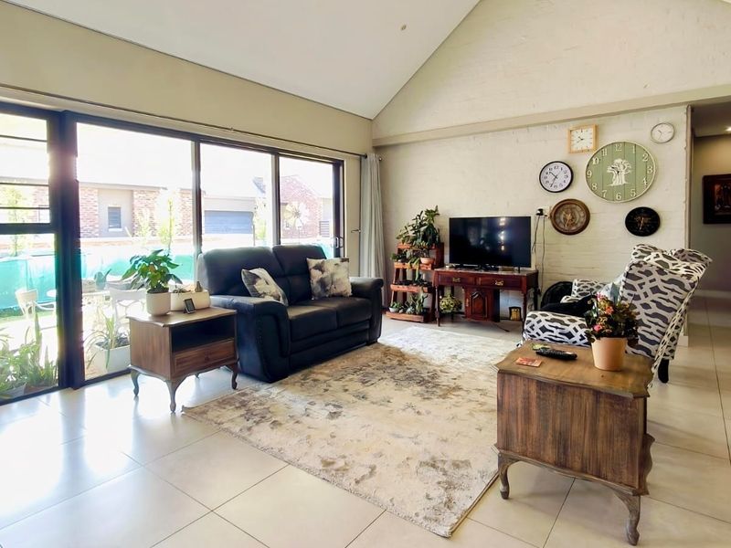 Spacious living room featuring a high vaulted ceiling, tiled flooring, and large sliding glass doors that provide ample natural light and garden access.