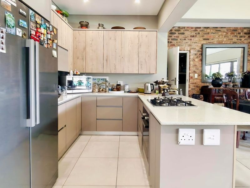 Modern open-plan kitchen featuring light wood and neutral cabinetry, stone countertops, gas hob, and an adjacent dining area with an exposed brick wall.