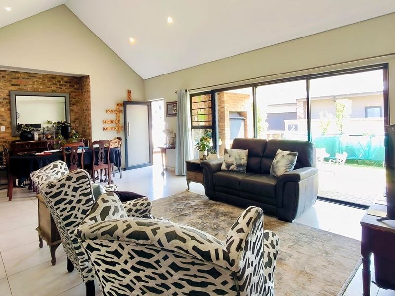 Spacious open-plan living area featuring a vaulted ceiling, exposed brick accent wall, and large sliding doors providing seamless access to the outdoor patio.