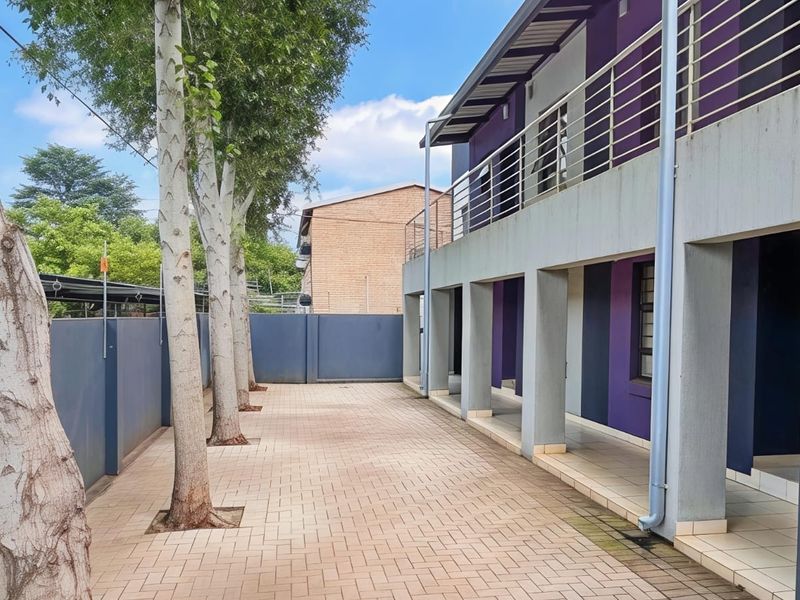 A paved rear courtyard area featuring a covered walkway, balcony with metal railings, and a boundary wall, providing functional outdoor space for the apartment.