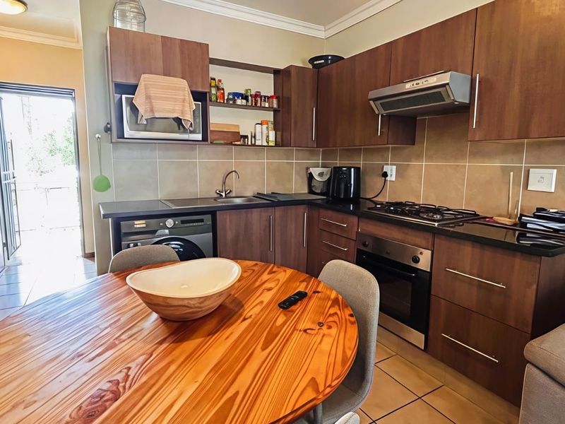 Open-plan kitchen featuring dark wood cabinetry, granite countertops, built-in gas hob, oven, and integrated laundry facilities, seamlessly connecting to the living area.