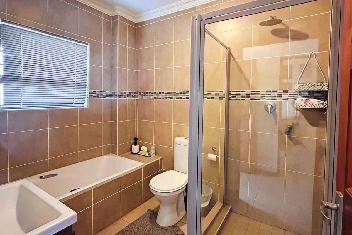 A well-maintained bathroom featuring a built-in bathtub, a separate glass-enclosed shower, and neutral wall tiling throughout.