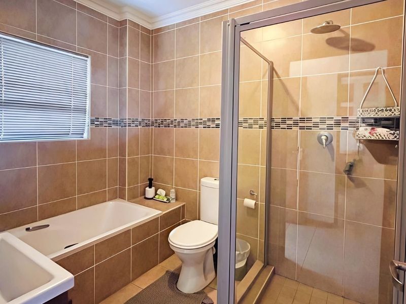A well-maintained bathroom featuring a built-in bathtub, a separate glass-enclosed shower, and neutral wall tiling throughout.