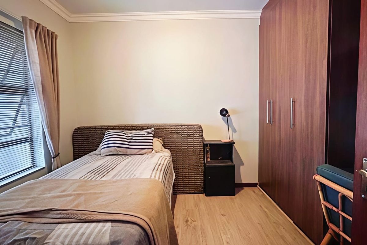 A well-maintained bedroom featuring light laminate flooring, neutral walls, and extensive floor-to-ceiling built-in wooden cupboards.