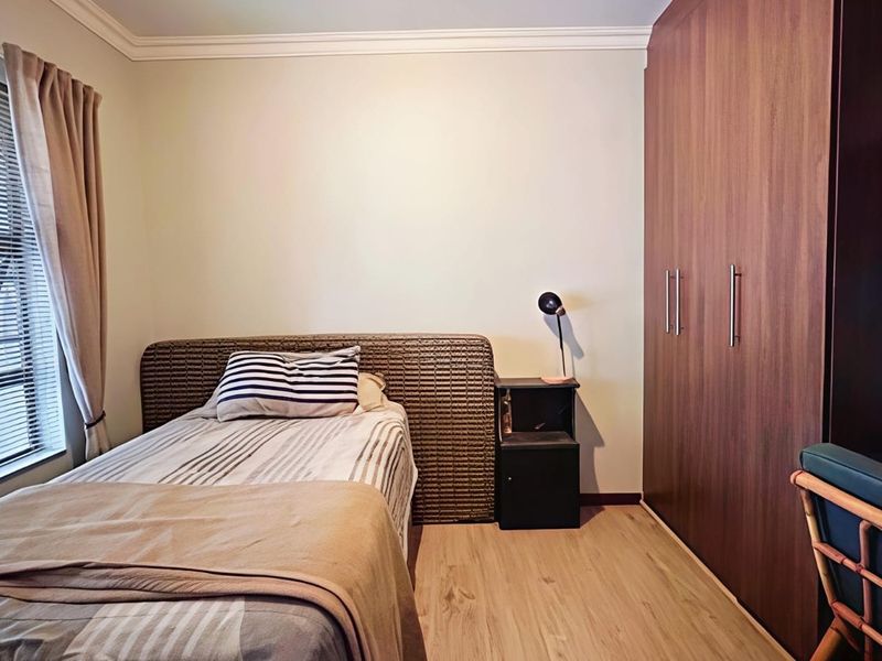 A well-maintained bedroom featuring light laminate flooring, neutral walls, and extensive floor-to-ceiling built-in wooden cupboards.