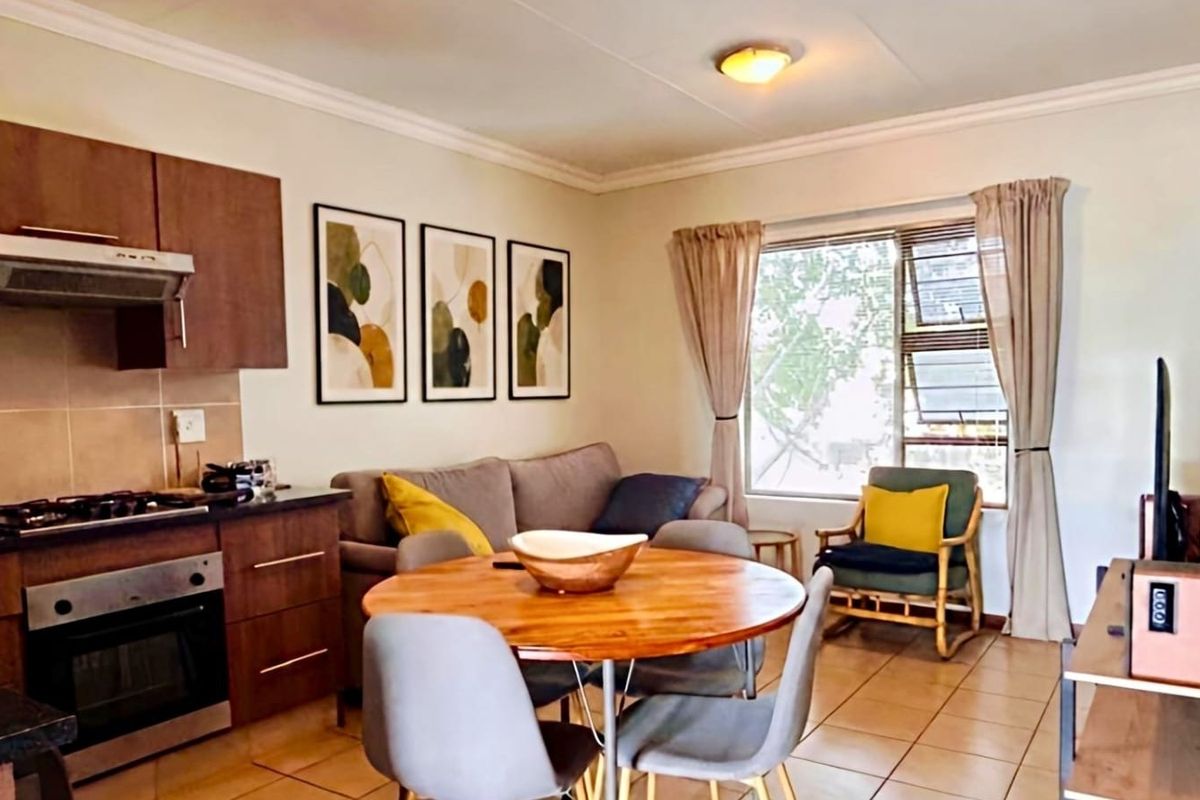 Open-plan living area featuring a functional kitchen with built-in cabinetry, oven, and hob, seamlessly flowing into a comfortable dining and lounge space.