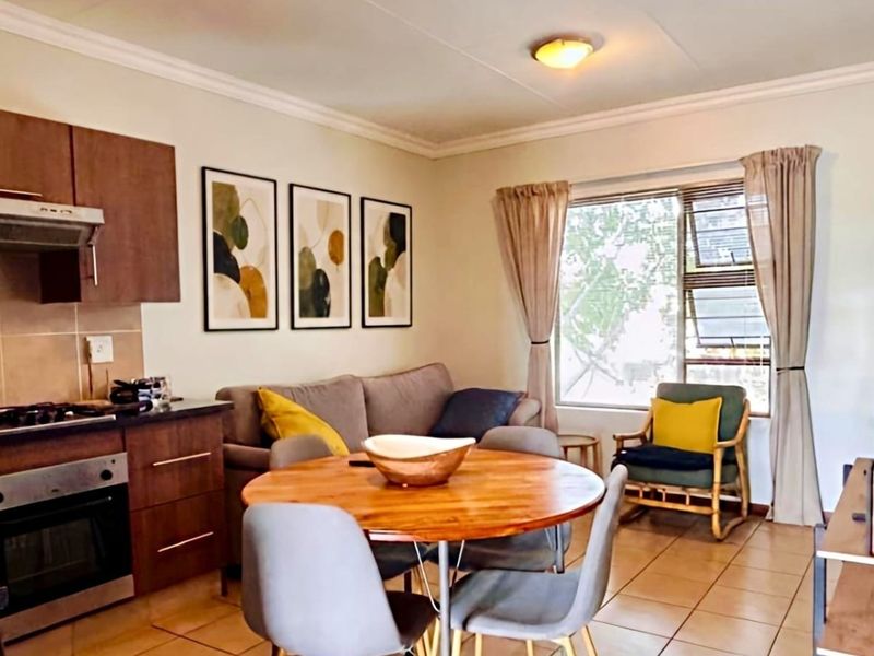 Open-plan living area featuring a functional kitchen with built-in cabinetry, oven, and hob, seamlessly flowing into a comfortable dining and lounge space.