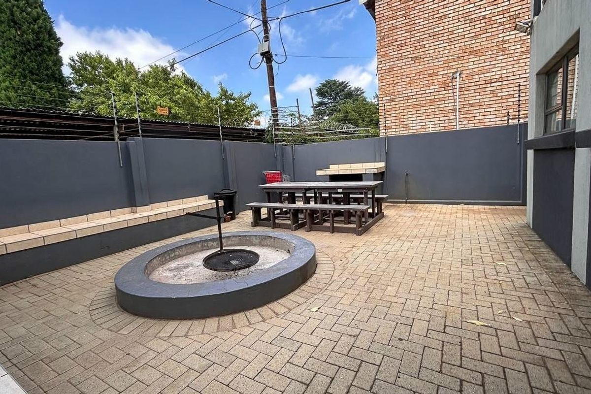 A paved rear courtyard featuring a built-in braai, circular fire pit, and perimeter wall with electric fencing for added security.
