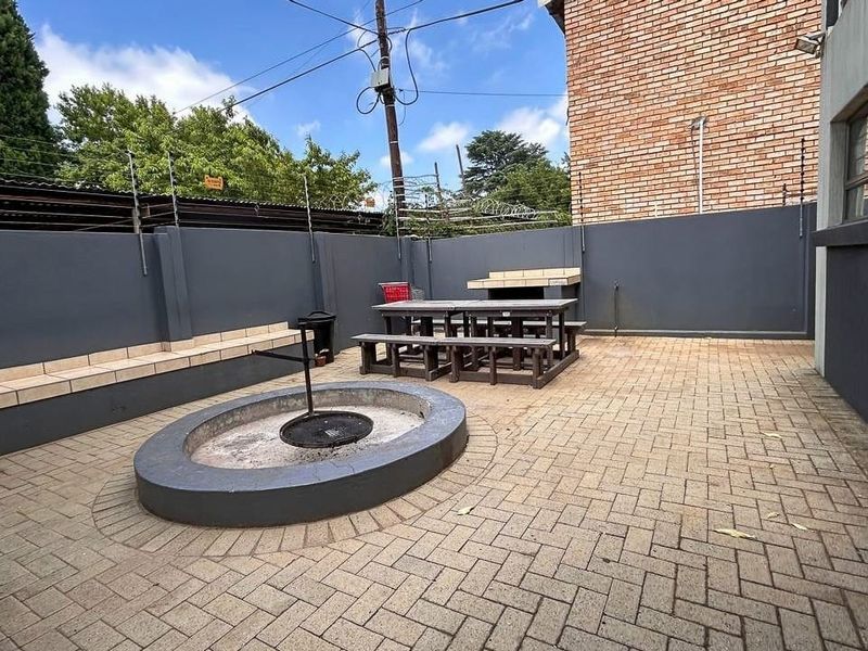 A paved rear courtyard featuring a built-in braai, circular fire pit, and perimeter wall with electric fencing for added security.