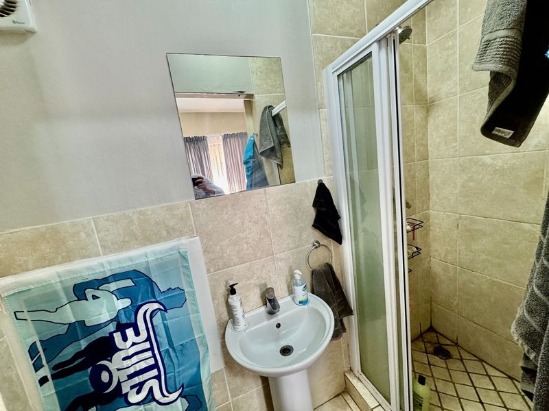 A compact bathroom featuring a pedestal basin, tiled walls, and a corner shower enclosure with a glass door.