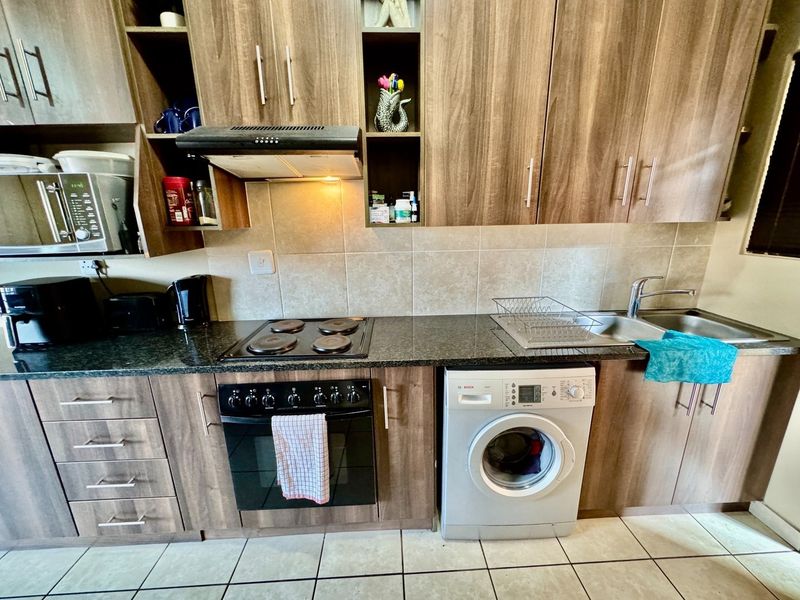 A functional kitchen featuring wood-finish cabinetry, granite countertops, a built-in oven with hob, extractor fan, and space for an under-counter washing machine.