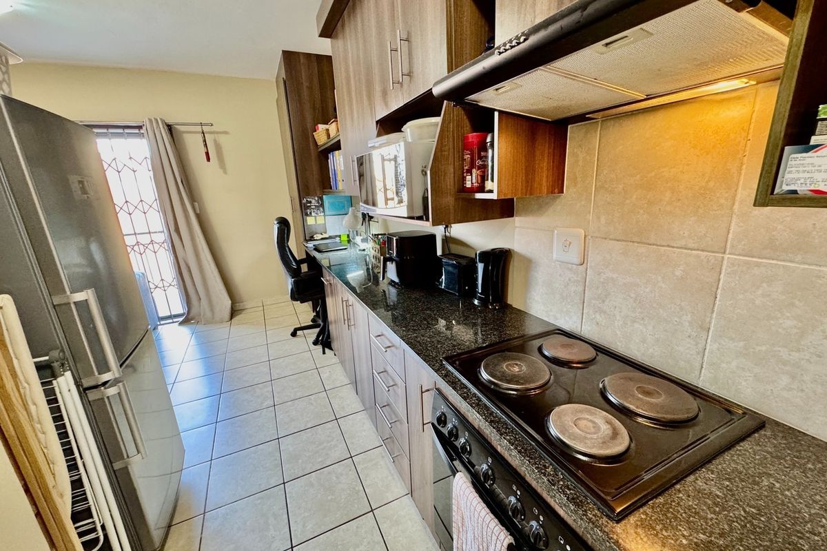 A functional kitchen featuring dark wood cabinetry, granite countertops, a built-in electric hob, oven, and extractor fan, with tiled flooring throughout.