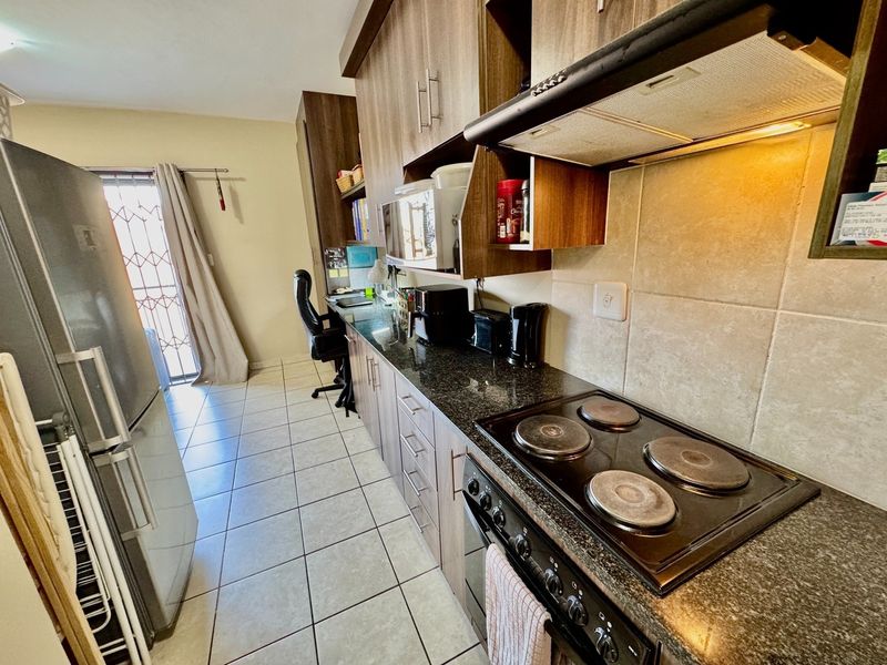 A functional kitchen featuring dark wood cabinetry, granite countertops, a built-in electric hob, oven, and extractor fan, with tiled flooring throughout.