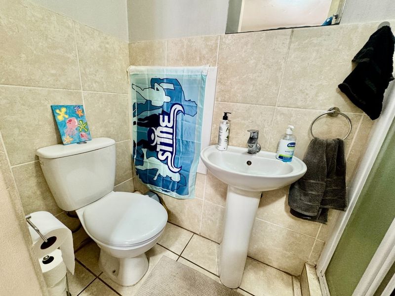 A compact bathroom featuring a pedestal basin, toilet, and neutral wall and floor tiling.