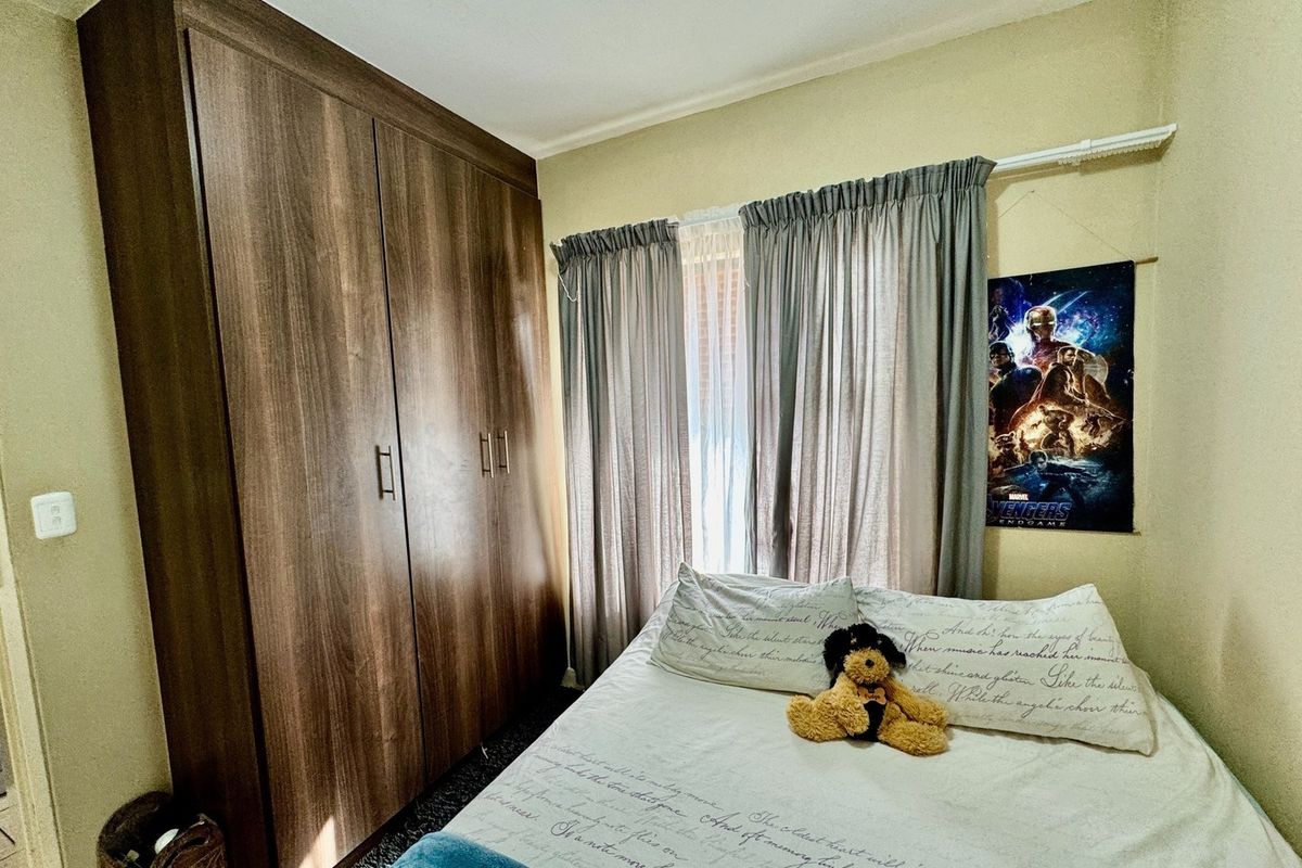 A bedroom featuring a large, dark wood-finish built-in wardrobe and window with installed curtain rails.