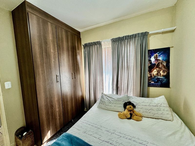A bedroom featuring a large, dark wood-finish built-in wardrobe and window with installed curtain rails.