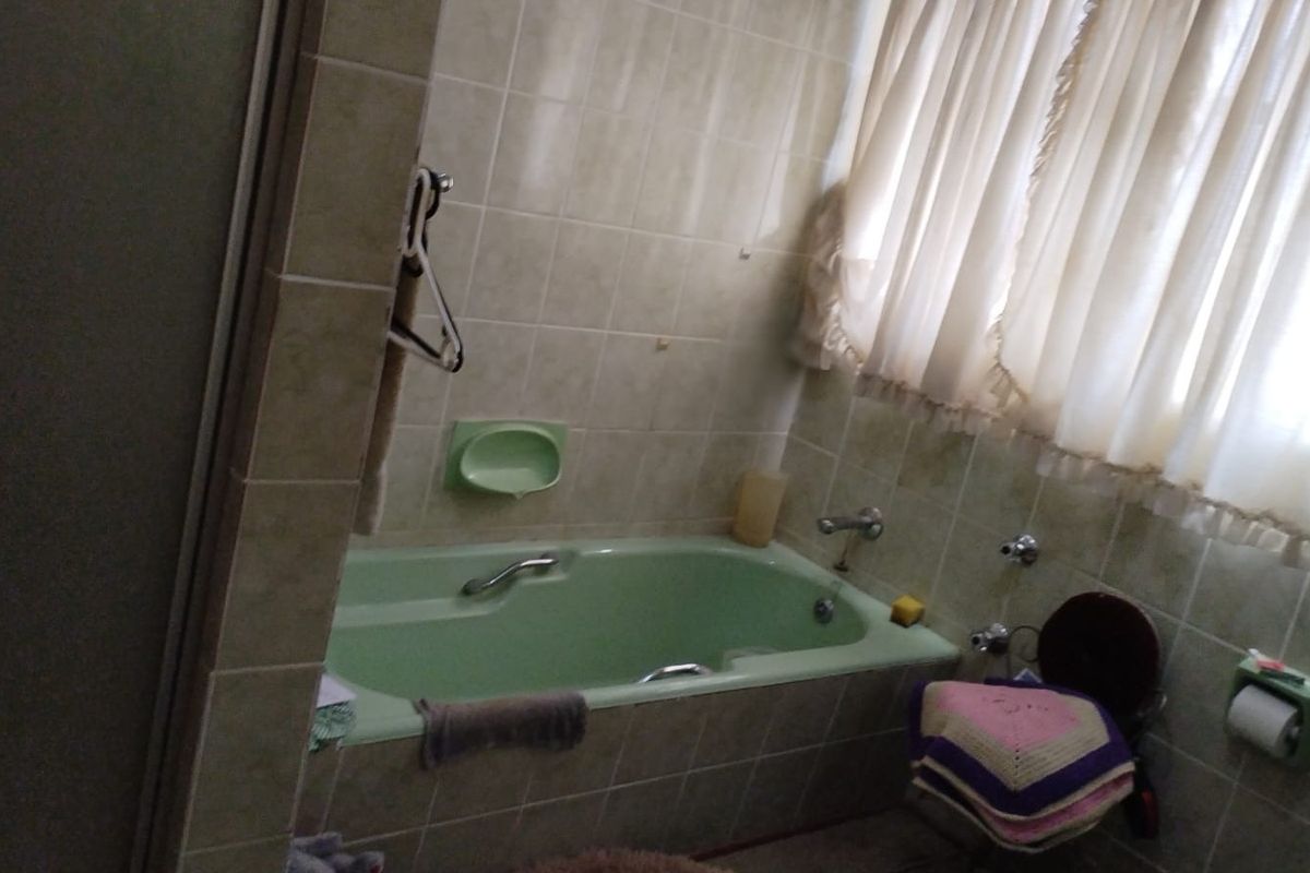 A dated bathroom featuring a built-in bathtub with tiled surround and walls, offering a functional space in need of modernization.