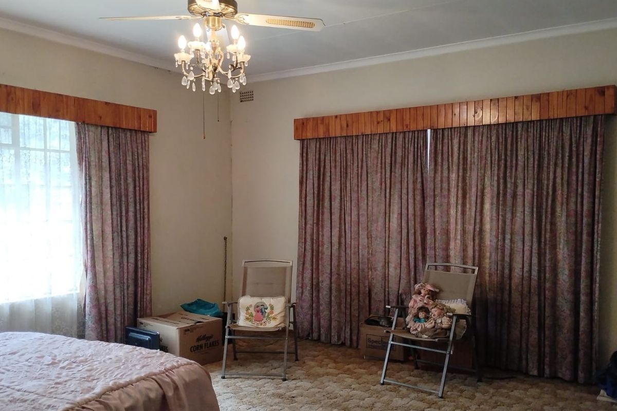 A bedroom featuring a ceiling fan, chandelier lighting, and wooden curtain pelmets over large windows.