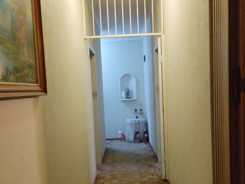 A narrow interior hallway featuring a built-in wall niche and a security gate, showing signs of dated finishes and wear.