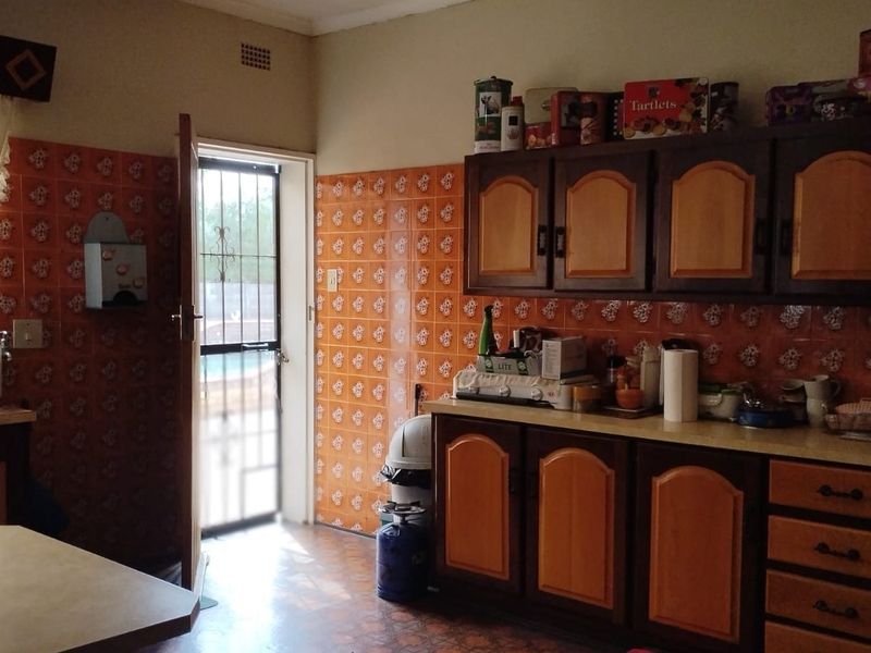 A dated kitchen featuring traditional wooden cabinetry, patterned tiled walls, and direct access to the exterior through a security gate.