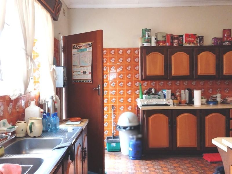A functional kitchen featuring timber cabinetry, laminate countertops, and a double bowl stainless steel sink with decorative tiled splashbacks.