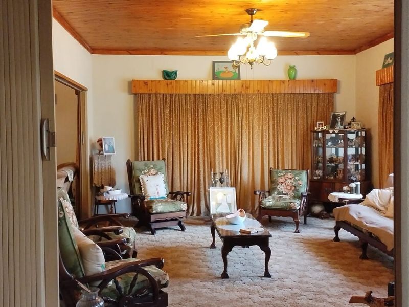 A traditional living room featuring a warm timber-clad ceiling, ceiling fan, and floor-to-ceiling curtains with a wooden pelmet.