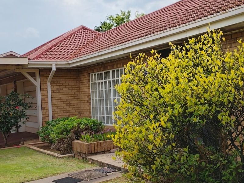 Front elevation of a face brick house featuring a tiled roof, carport, and established garden area.