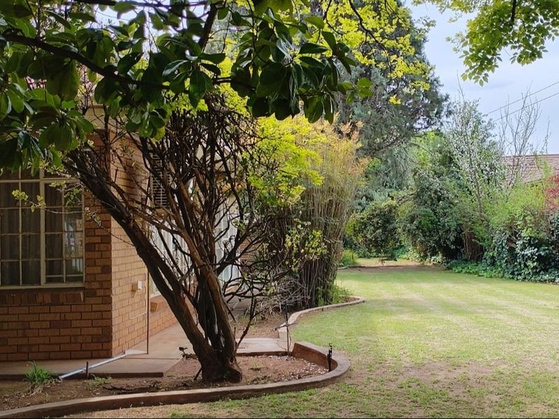 A spacious backyard featuring a well-maintained lawn, mature trees, and a brick exterior wall of the house.