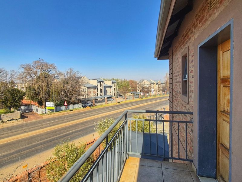 A private balcony featuring tiled flooring, a metal safety railing, and direct access to the apartment via a timber door, overlooking the street.